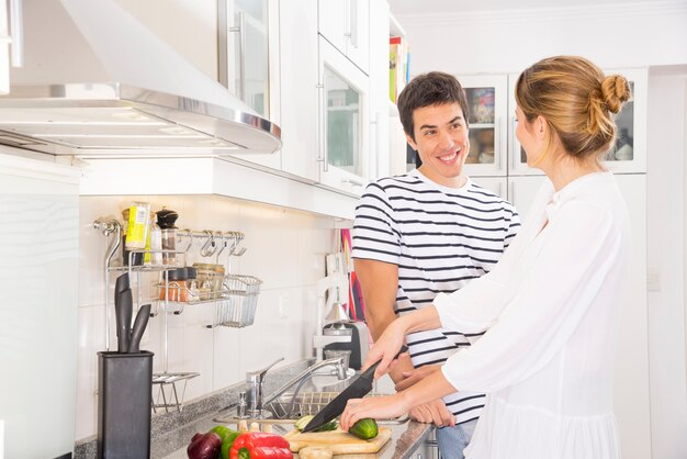 Homme souriant, regardant une femme coupant des légumes avec un couteau tranchant