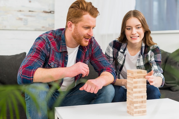 Homme souriant en regardant une femme jouant à la pile de blocs de bois à la maison