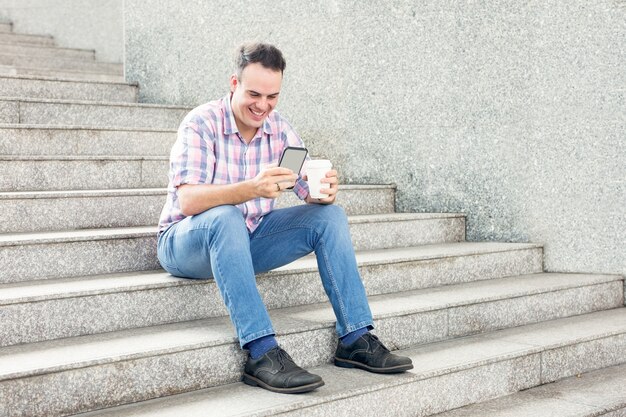 Homme souriant avec Smartphone et boisson sur l&#39;escalier