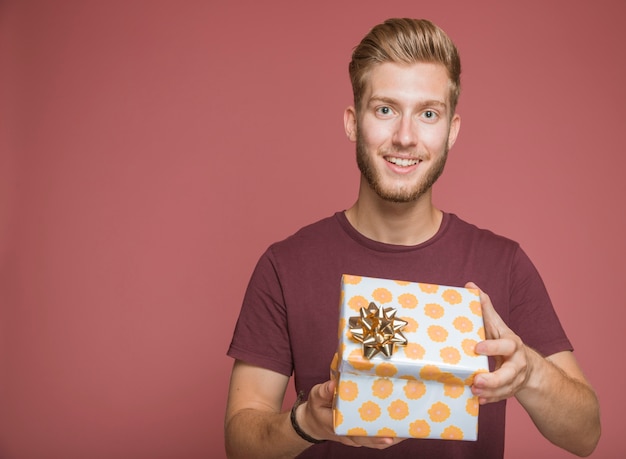 Photo gratuite homme souriant, tenant boîte cadeau enveloppé sur fond coloré