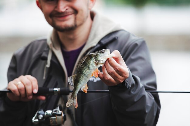 Homme souriant, tenant la canne à pêche montrant des poissons capturés