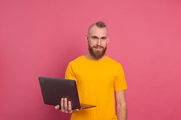 Homme souriant travaillant avec un ordinateur portable isolé sur fond rose