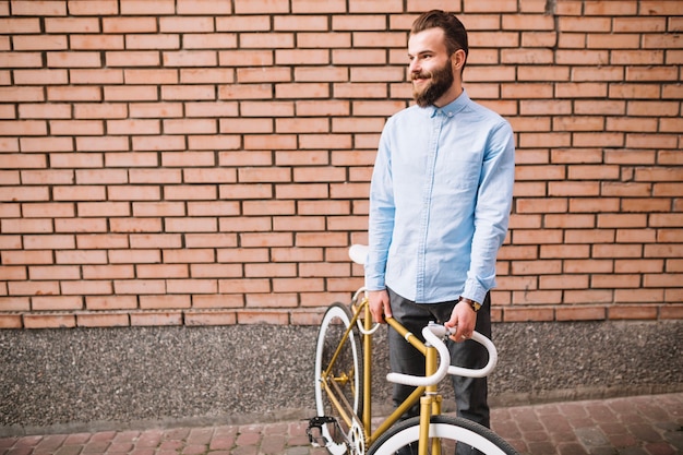 Homme souriant avec vélo près du mur de briques