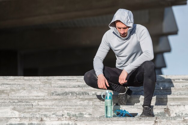 Homme sportif assis dans les escaliers et en regardant une bouteille d'eau