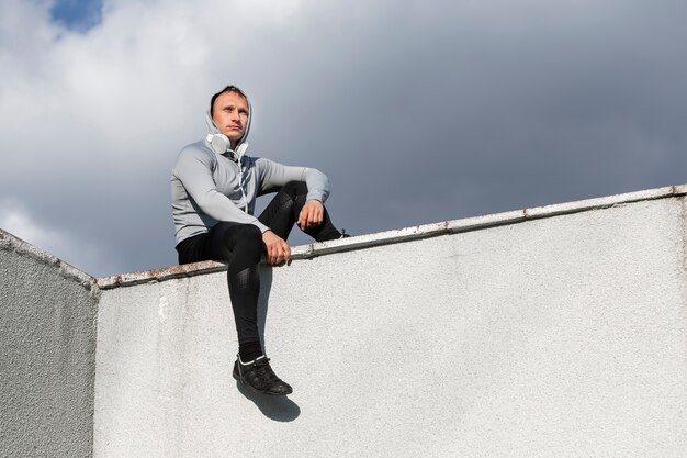 Homme sportif assis sur un mur et regardant au loin
