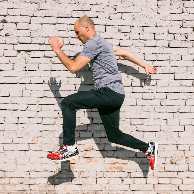 Homme sportif athlète jeune sautant dans les airs contre un mur peint blanc