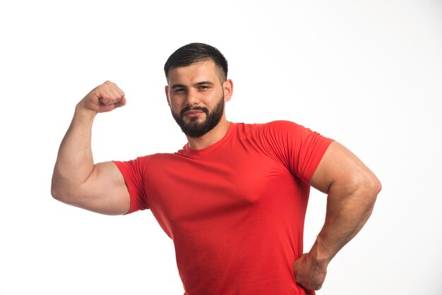 Homme sportif en chemise rouge démontrant ses muscles du bras et a l'air confiant