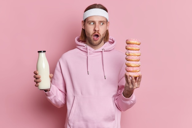 Un homme sportif étonné regarde de délicieux beignets savoureux a envie de manger vêtu d'un bandeau blanc à capuche.