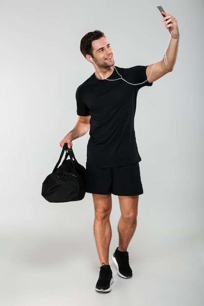 Homme sportif gai faire selfie avec sac par téléphone mobile