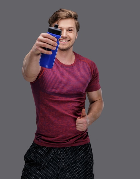 Homme sportif positif avec une bouteille d'eau. isolé sur gris