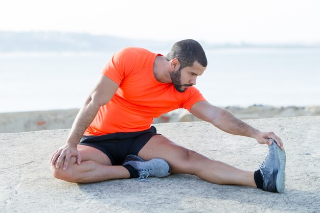 Un homme sportif sportif bien concentré qui étire les jambes en plein air