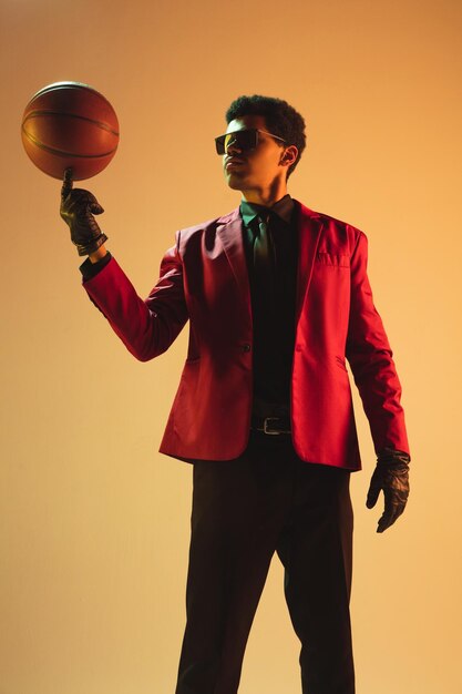 Homme de style haute couture en veste rouge jouant au basket isolé sur fond marron