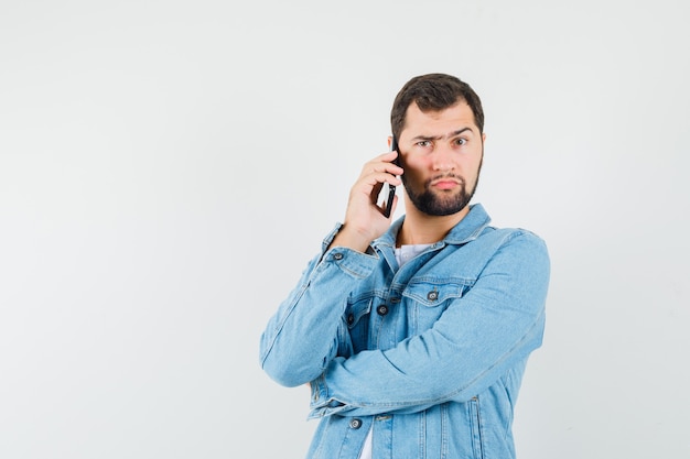 Homme de style rétro parlant au téléphone en veste, t-shirt et regardant pensif, vue de face.