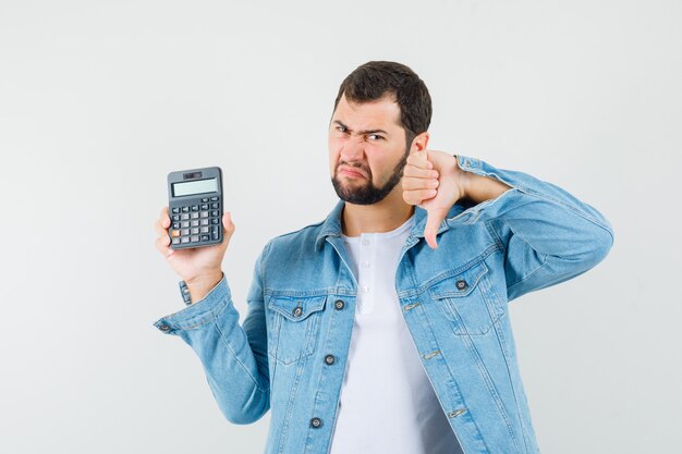 Homme de style rétro tenant une calculatrice tout en montrant le pouce vers le haut en veste, t-shirt et à la recherche d'insatisfait. vue de face.