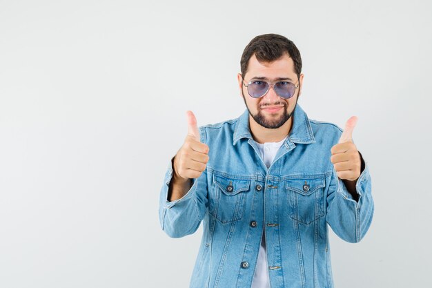 Homme de style rétro en veste, lunettes de soleil montrant le pouce vers le haut et impressionnant, vue de face.