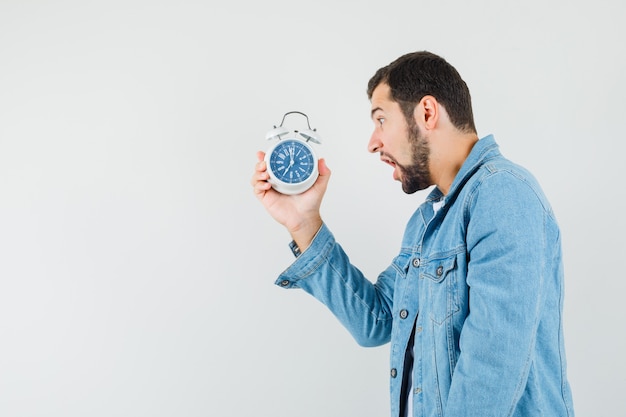 Homme De Style Rétro En Veste, T-shirt Tenant Une Horloge Et Regardant Troublé.