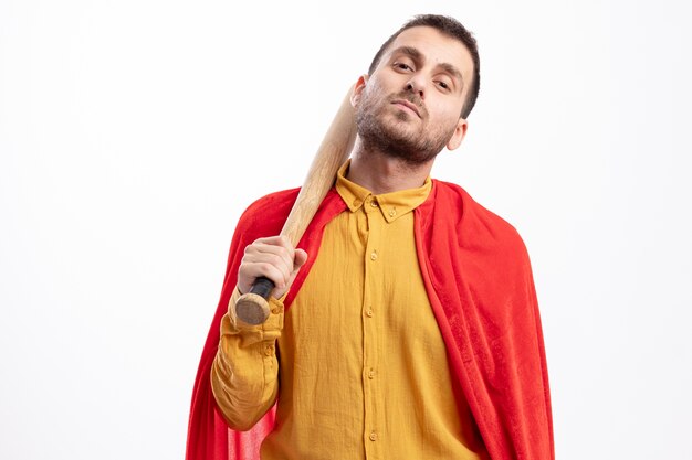 Homme de super-héros caucasien confiant avec manteau rouge tient une batte de baseball sur l'épaule sur blanc