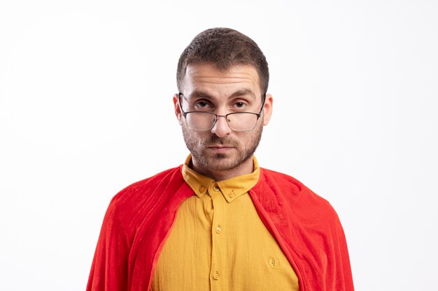 Homme de super-héros confiant dans des lunettes optiques avec manteau rouge regarde à l'avant isolé sur mur blanc