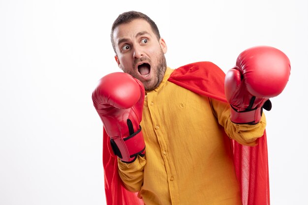 Homme de super-héros effrayé se tient avec des gants de boxe isolés sur un mur blanc
