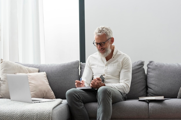 Homme supérieur à la maison étudiant sur ordinateur portable et prenant des notes