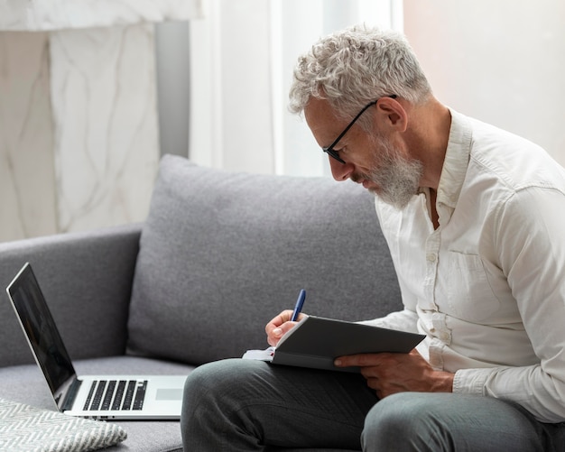 Photo gratuite homme supérieur à la maison étudiant sur ordinateur portable et prenant des notes