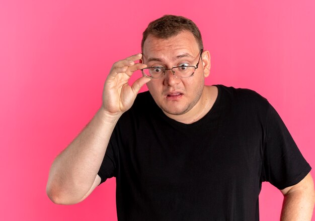 Homme en surpoids à lunettes portant un t-shirt noir lookign à quelque chose de surpris et étonné de rose