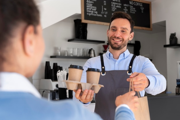 Homme avec tablier offrant des plats à emporter emballés à une cliente