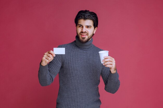 Homme avec une tasse de café montrant sa facture ou sa carte de visite.