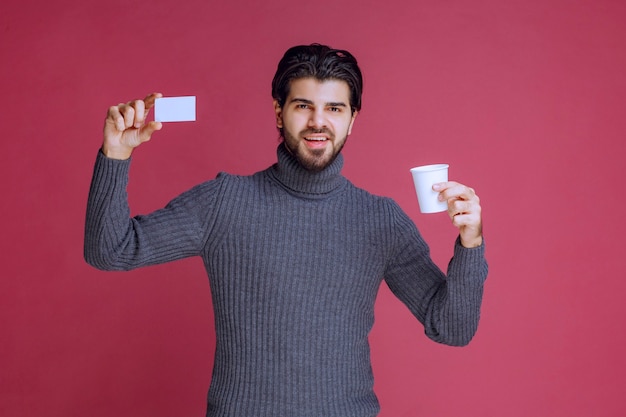 Homme avec une tasse de café montrant sa facture ou sa carte de visite.