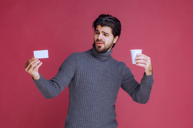 Homme avec une tasse de café montrant sa facture ou sa carte de visite.