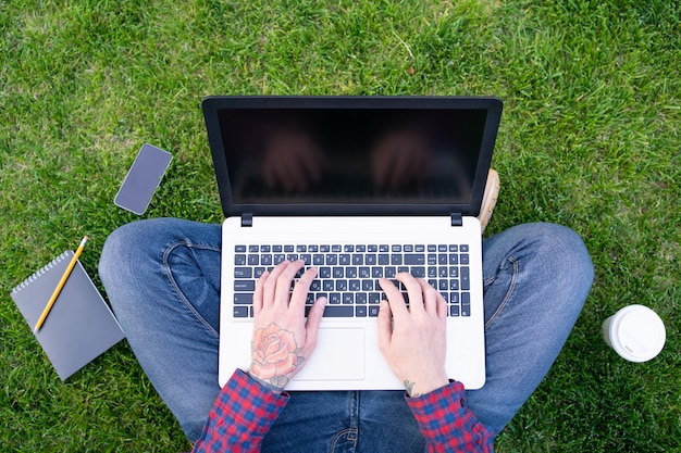 Homme avec tatouage rose sur la main en tapant sur un ordinateur portable