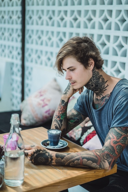 un homme tatoué boit un café coloré dans un café.