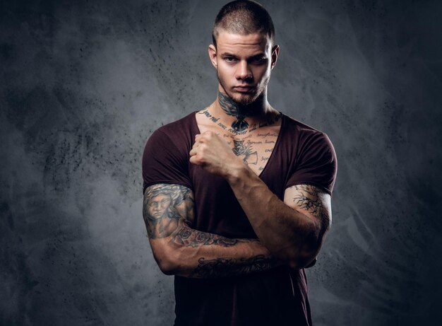 Homme tatoué avec les bras croisés sur fond artistique gris.