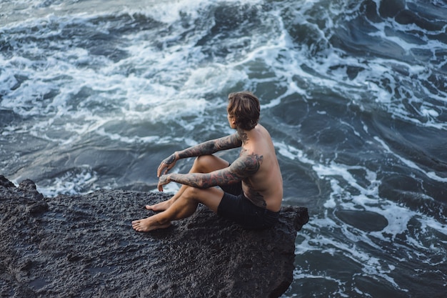 Un homme tatoué repose sur le bord d&#39;une falaise. éclaboussures d&#39;ondes océaniques.