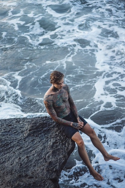 Un homme tatoué repose sur le bord d&#39;une falaise. éclaboussures d&#39;ondes océaniques.