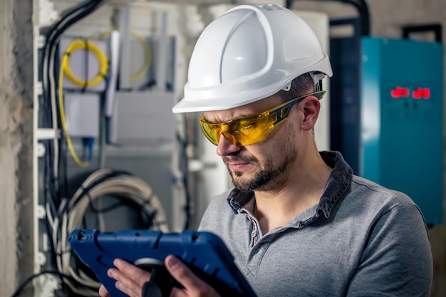 L'homme un technicien électricien travaillant dans un standard avec des fusibles utilise une tablette