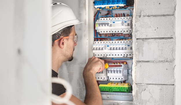 Homme, technicien électricien travaillant dans un tableau avec fusibles. Installation et connexion d'équipements électriques.