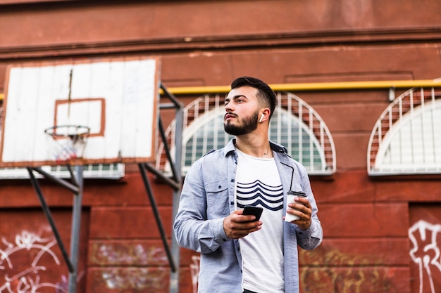 Homme avec téléphone portable debout dans le terrain de basket