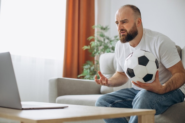 Photo gratuite homme tenant un ballon de football et regardant le football en ligne à la maison