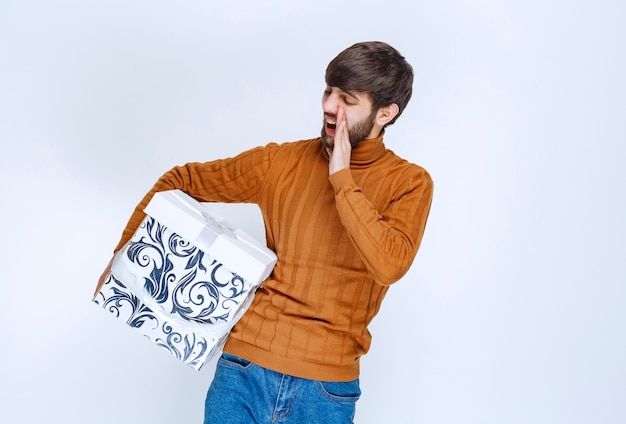 Homme tenant une boîte-cadeau blanche avec des motifs bleus faisant du bruit pour remarquer quelqu'un.