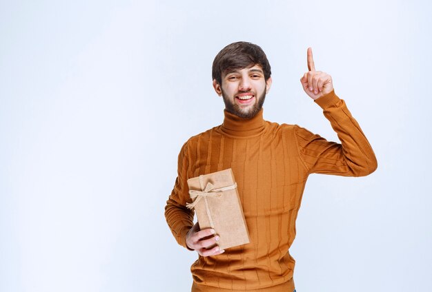 Homme tenant une boîte-cadeau en carton et pointant quelque chose à l'envers.