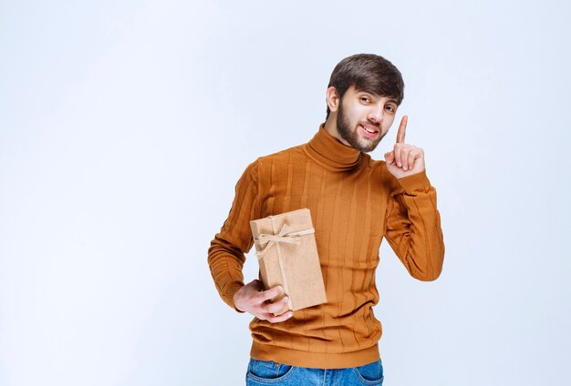 Homme tenant une boîte-cadeau en carton et pointant quelque chose à l'envers.