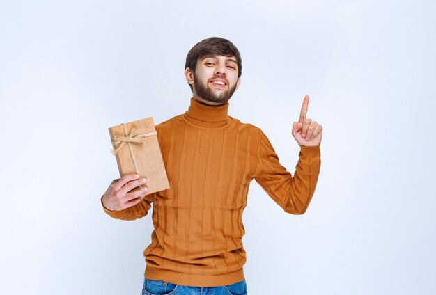 Homme tenant une boîte-cadeau en carton et pointant quelque chose à l'envers.