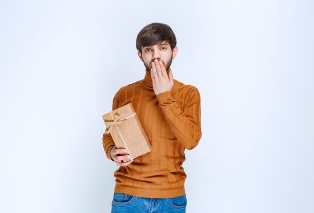 Homme tenant une boîte-cadeau en carton et semble confus et hésitant.