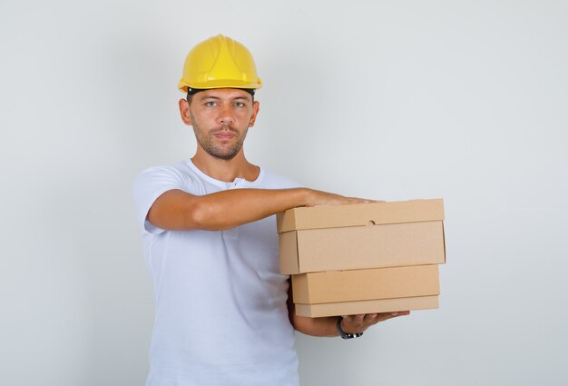 Homme tenant des boîtes en carton en t-shirt blanc, casque, vue de face.