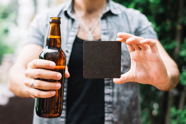 Homme tenant une bouteille de bière brune et une carte vierge noire dans les mains