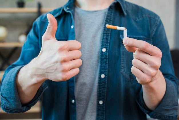 Photo gratuite homme tenant une cigarette cassée et montrant le pouce vers le haut de geste