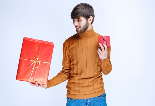 Homme tenant des coffrets cadeaux rouges grands et petits dans les deux mains.