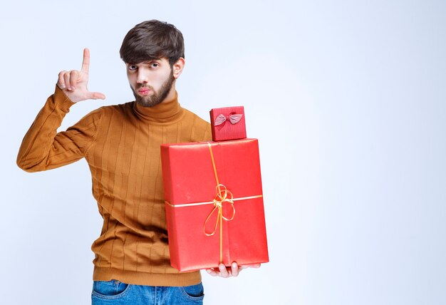 Homme tenant des coffrets cadeaux rouges grands et petits et montrant la taille en main.