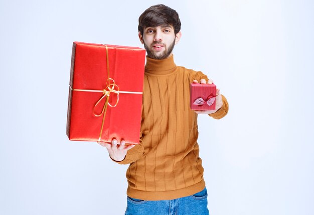 Homme tenant des coffrets cadeaux rouges grands et petits et offrant l'un d'eux à sa petite amie.